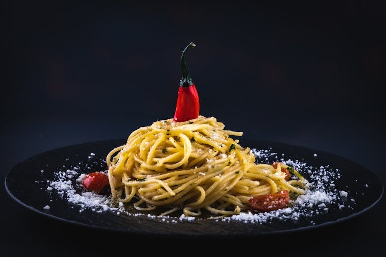 A beautifully styled plate of spaghetti with chili pepper on a black dish, garnished with cheese.