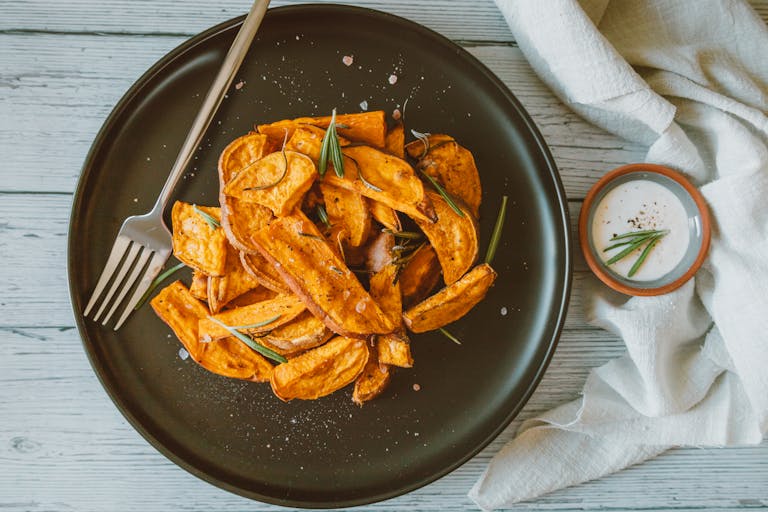 A delicious serving of crispy sweet potato fries garnished with rosemary on a black ceramic plate.