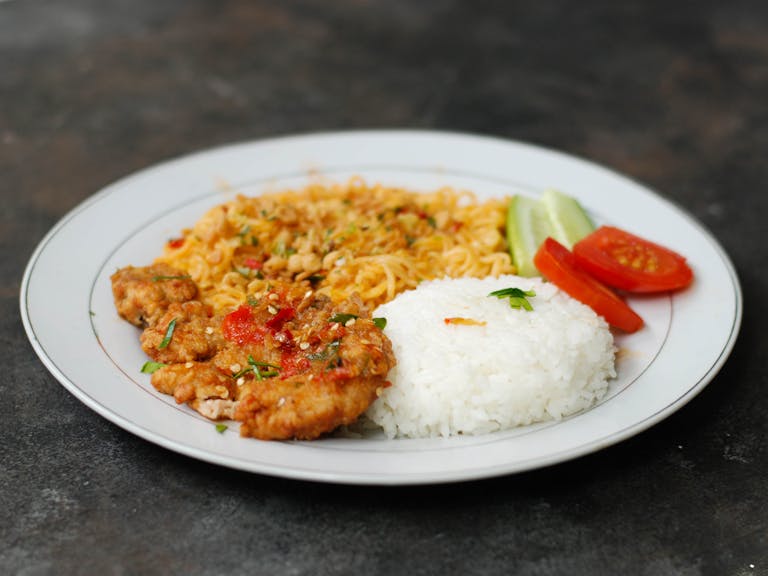 A mouth-watering plate of Indonesian ayam geprek served with spicy noodles and white rice.