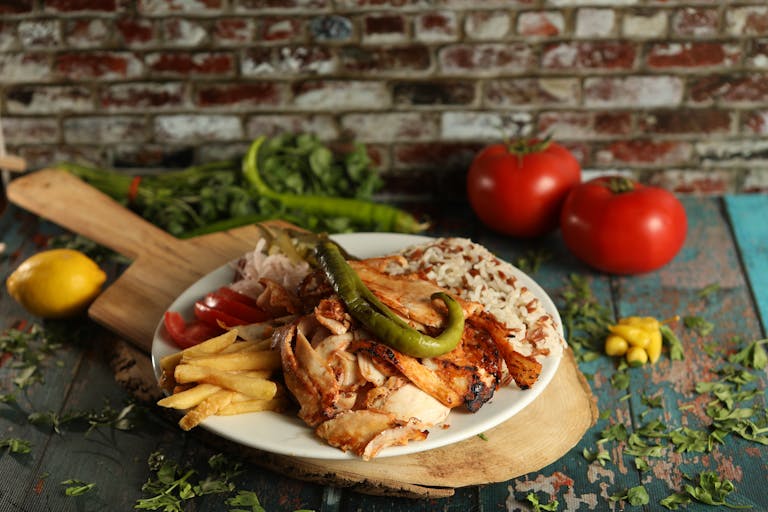 A mouthwatering plate of Turkish doner kebab with fries, rice, and vegetables in a rustic setting.