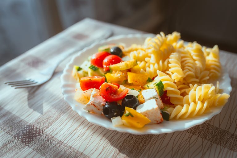 A vibrant plate of fusilli pasta with fresh tomatoes, olives, and feta cheese.