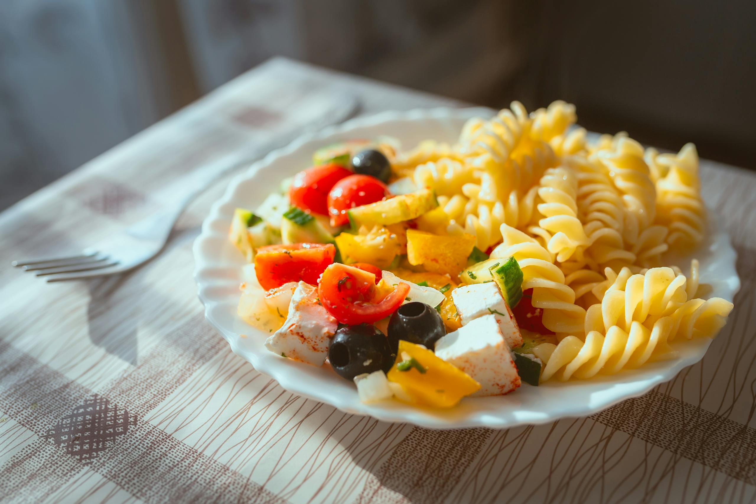 A vibrant plate of fusilli pasta with fresh tomatoes, olives, and feta cheese.