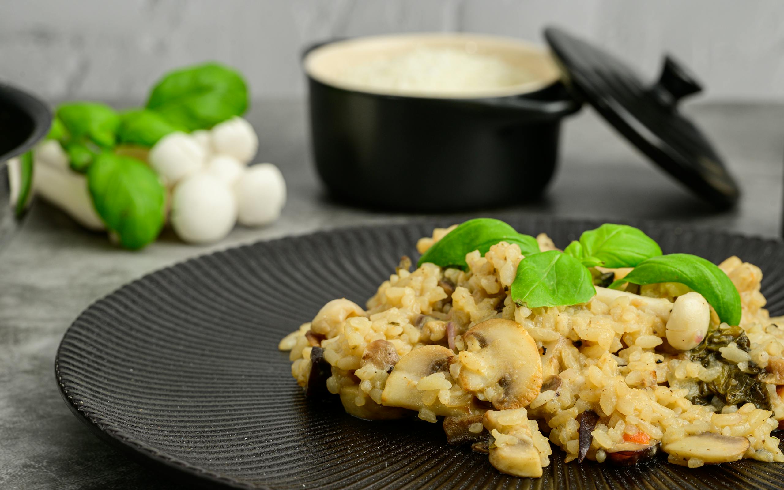 Close-up of creamy mushroom risotto topped with basil on a black plate, perfect for foodies.