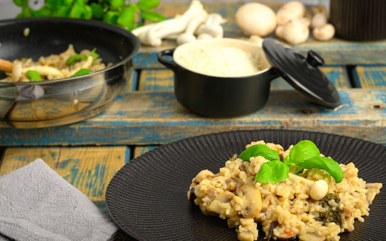 Close-up of creamy mushroom risotto with rice and basil, styled on a rustic wooden table.
