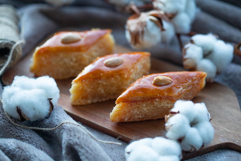 Close-up of sweet Turkish baklava pieces with almonds, surrounded by cotton flowers on a tray.