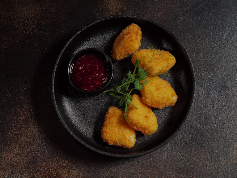 Golden fried nuggets served with a tangy dipping sauce on a black plate, garnished with fresh herbs.