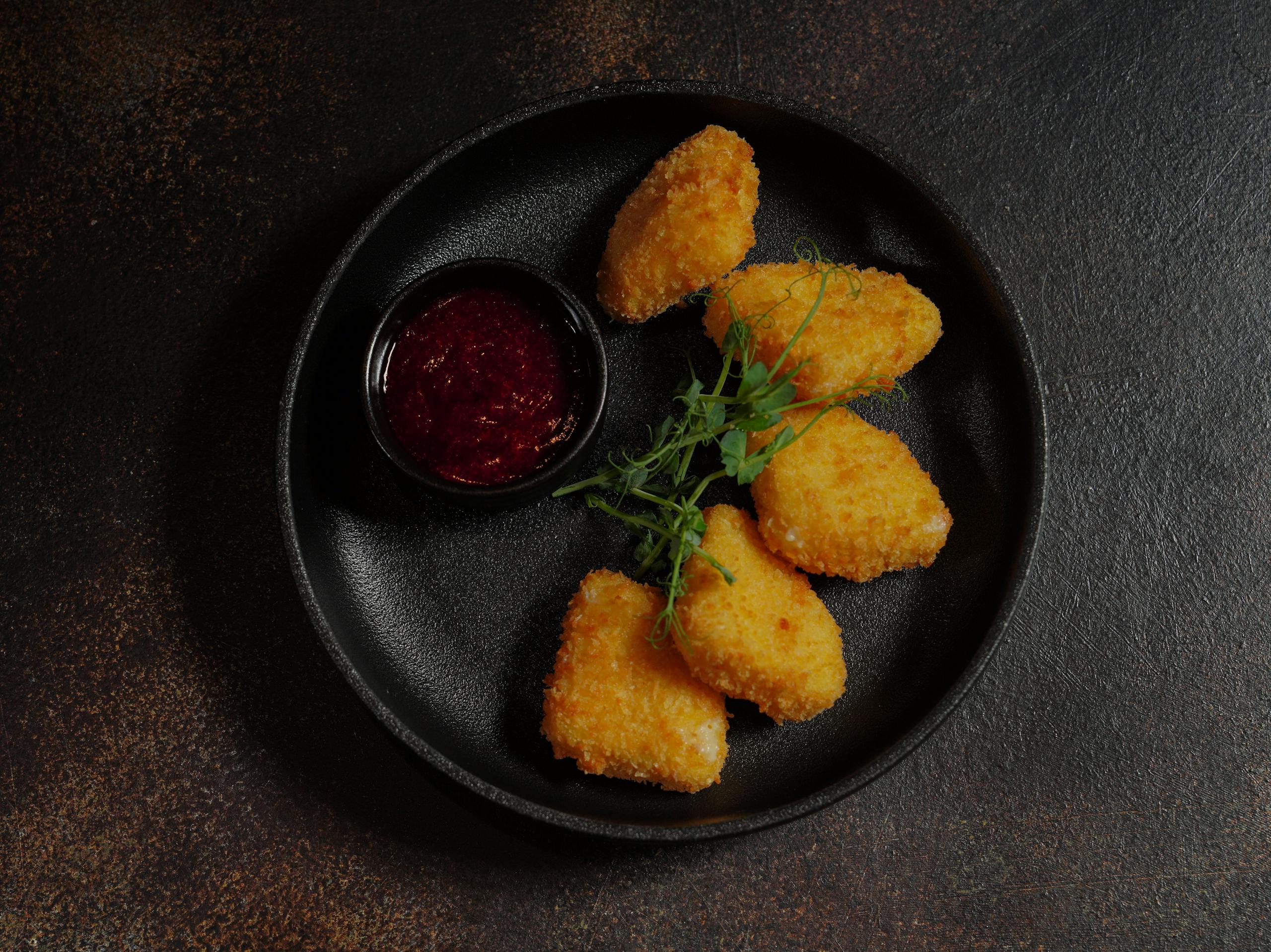 Golden fried nuggets served with a tangy dipping sauce on a black plate, garnished with fresh herbs.