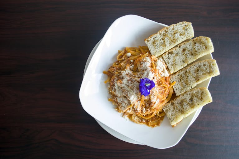Plate of spaghetti with parmesan and garlic bread on a wooden table.