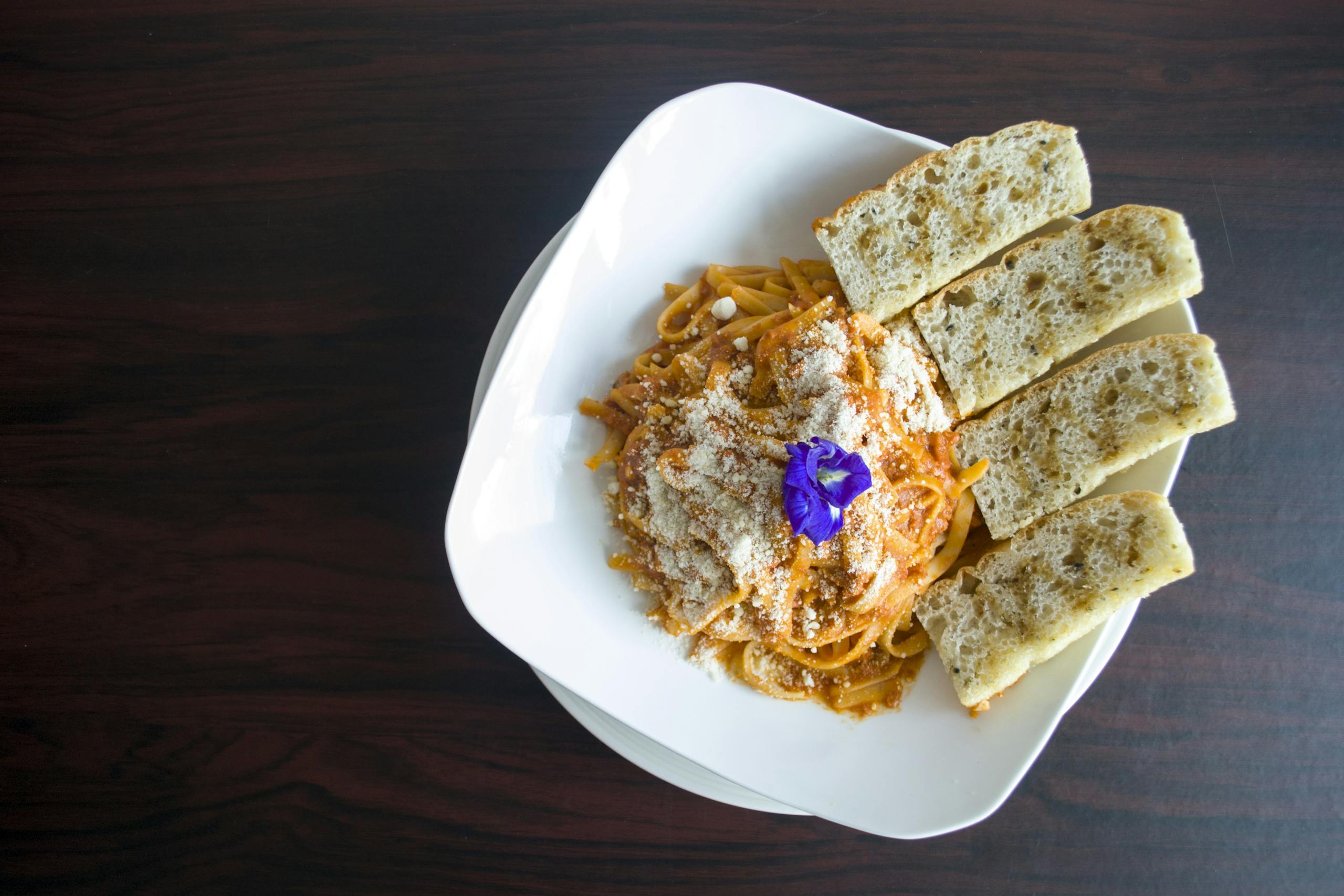 Plate of spaghetti with parmesan and garlic bread on a wooden table.